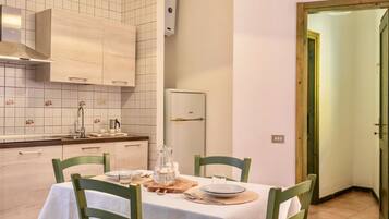 Un coin repas avec une table dressée pour deux personnes, une cuisine aux carreaux blancs et aux meubles en bois, et une porte donnant sur une autre pièce.