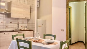 A dining area with a table set for two, a kitchen with white tiles and wooden cabinets, and a door leading to another room.