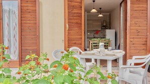 An open wooden door leading to a dining area with a table set for two, surrounded by white plastic chairs. - (45 sq m): living room with induction cooker, double sofa bed, double bedroom, bathroom. <br>The apartments are equipped with: <br>iron and ironing board (on request), <br><b>air conditioning</b>, <br>kitchenette with induction hob <br>tv <br>microwave,  (Santa Teresa di Gallura)
