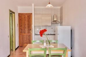 Een keuken met een houten deur, een witte betegelde spatwand en een eethoek met tafel en stoelen.