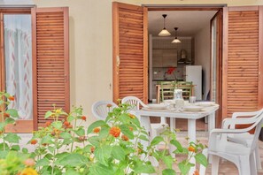 An open wooden door leading to a dining area with a table set for two, surrounded by white plastic chairs.