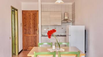 Una cocina con puerta de madera, salpicadero de azulejos blancos y una zona de comedor con mesa y sillas.