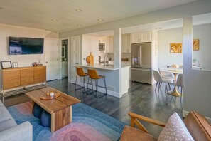 A modern living room with a sofa, a coffee table, and a TV. There is a kitchen area with a dining table and chairs. - Comfy Cute Condo - entire home (Boulder)