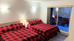 Une chambre d’hôtel avec deux lits, une fenêtre avec des rideaux, une lampe et une vue sur un espace extérieur enneigé.
