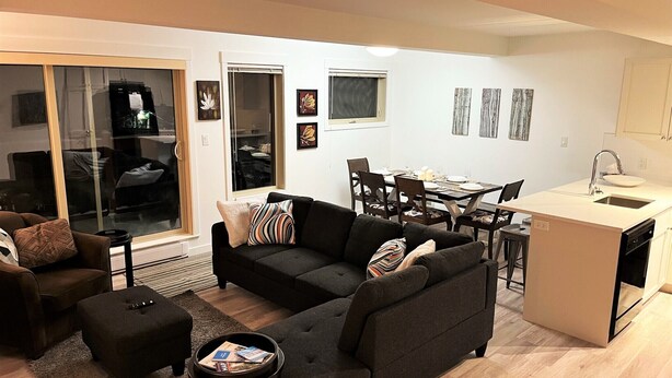 Un salon moderne avec un canapé gris foncé, une petite table basse et un coin repas comprenant une table et des chaises blanches.