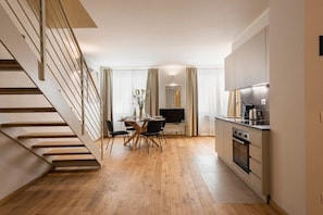 Una cocina moderna con suelo de madera, un comedor con mesa y sillas, y una escalera.