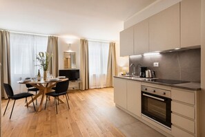 A modern kitchen with a dining area, wooden flooring, and a large window with curtains.