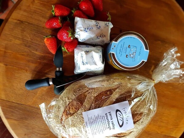 A wooden table with a loaf of bread, a jar of jam, a packet of cheese, and fresh strawberries.