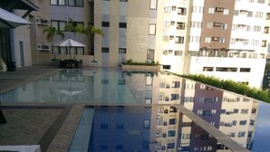 A modern outdoor swimming pool with clear water, surrounded by a stone deck and low-rise buildings in the background. - Stunning Studio Type - 1641 - 16th Flr Persimmon (Cebu)