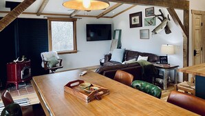 Un salon chaleureux avec une table à manger en bois, des fauteuils en cuir, une cheminée et un téléviseur fixé au mur.