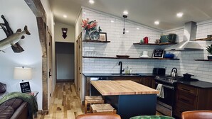 Une cuisine moderne avec des carreaux de céramique blancs disposés en motif métro, des plans de travail en bois et une cuisinière intégrée. On y trouve également un coin repas avec une table en bois et des chaises en cuir.