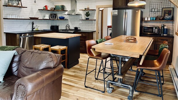 Une cuisine moderne dotée d’un îlot central, de planchers en bois et d’un coin repas avec des tabourets.