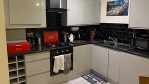Una cocina moderna con estufa negra, armarios blancos y un panera roja.