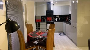 Una cocina compacta con electrodomésticos modernos, una mesa de comedor con cuatro sillas y un mantel individual rojo.
