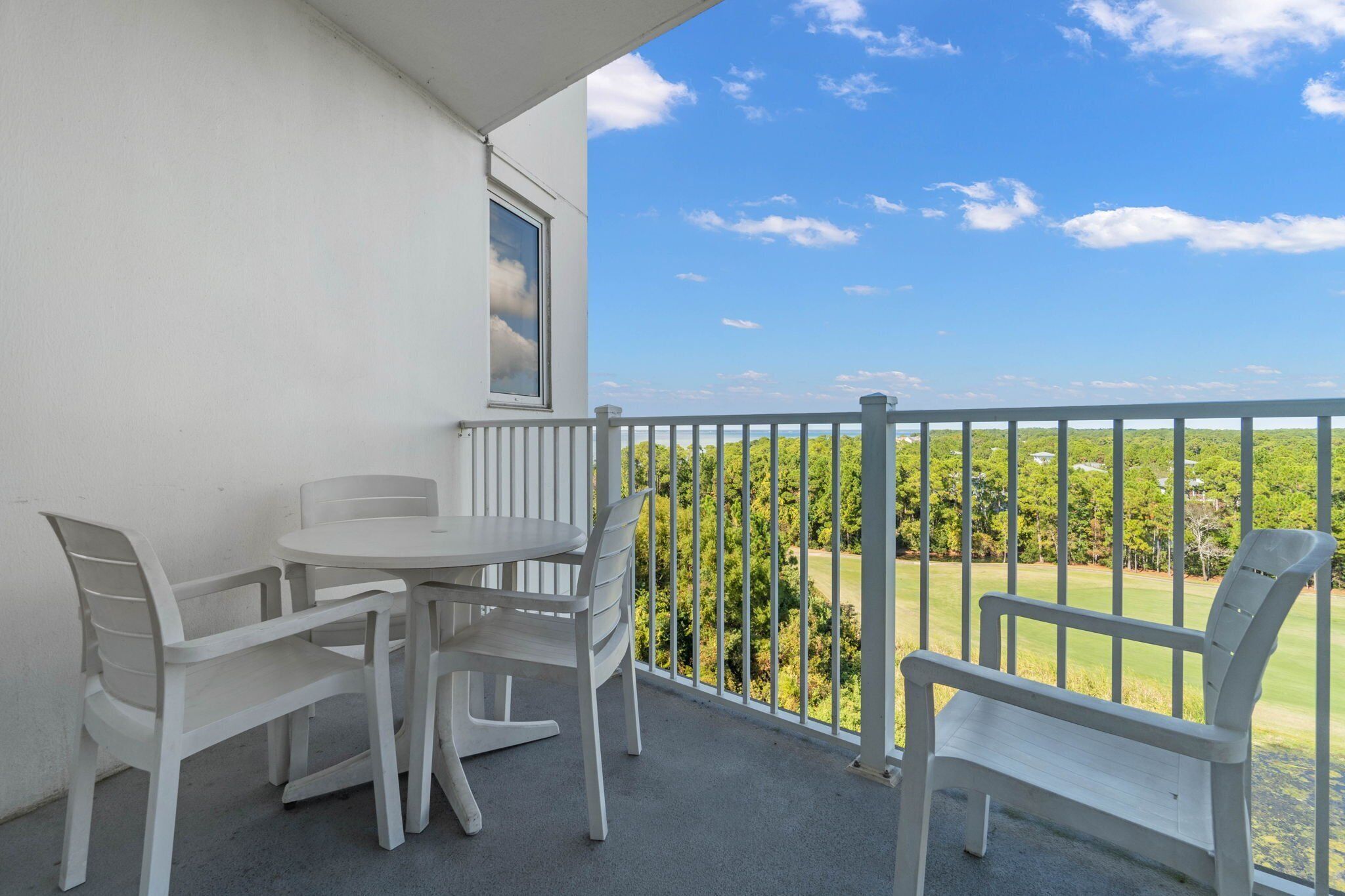 Un balcón con una mesa y sillas blancas, un banco blanco y vistas a un paisaje verde.