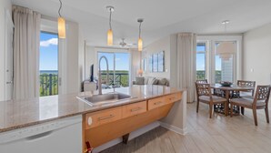Una cocina moderna con una isla grande, un comedor con mesa y sillas, y ventanas amplias que ofrecen vistas al exterior.