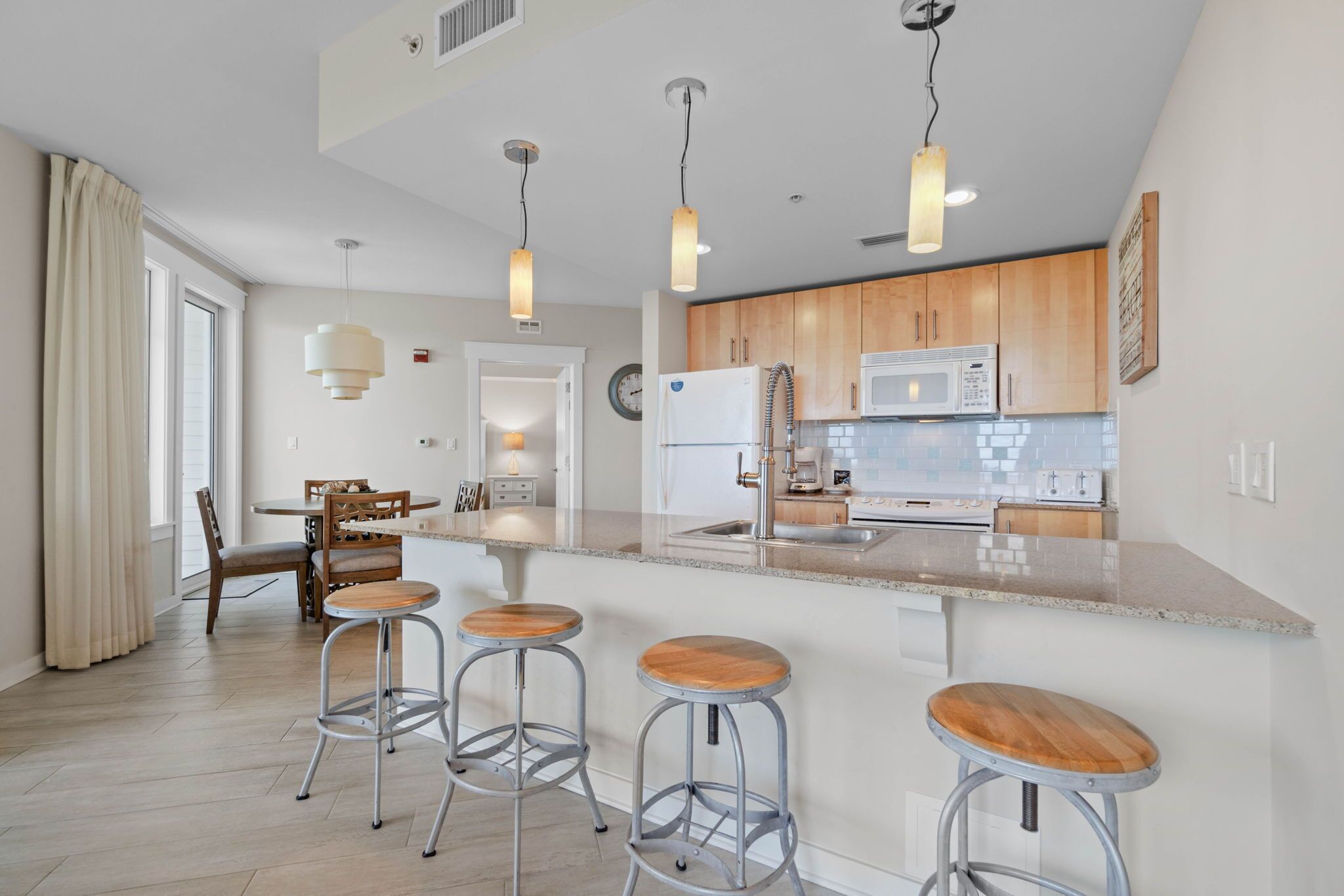 A modern kitchen with wooden cabinets, a large island with stools, stainless steel appliances, and pendant lighting.
