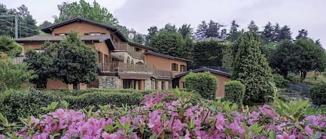 A two-story house with a balcony and a garden with pink flowers.