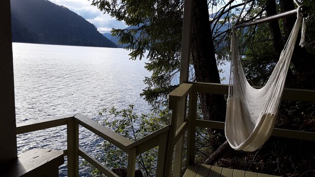 A hammock hanging on a wooden deck overlooking a lake with mountains in the background.