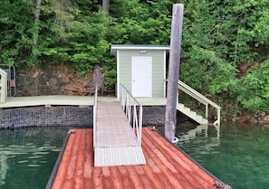 Guests can access the waterfront from a wooden dock with a metal handrail, leading to a charming building with a white door.