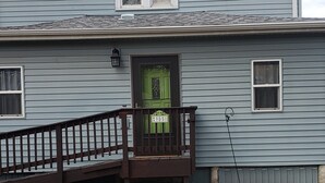 Una casa de dos pisos con una puerta verde en la parte delantera, un pequeño porche y un techo gris.