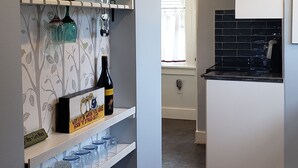 Una cocina moderna con muebles blancos, un salpicadero de azulejos negros y un ventanal con cortinas blancas.