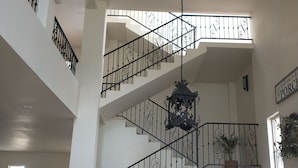 Ein großzügiger Wohnbereich mit hoher Decke, einer Treppe mit aufwendiger schwarzer Geländer und einem Esstisch mit Stühlen.