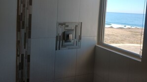 Ein Badezimmer mit Dusche, einem Fenster mit Blick auf den Strand und einer gefliesten Wand.