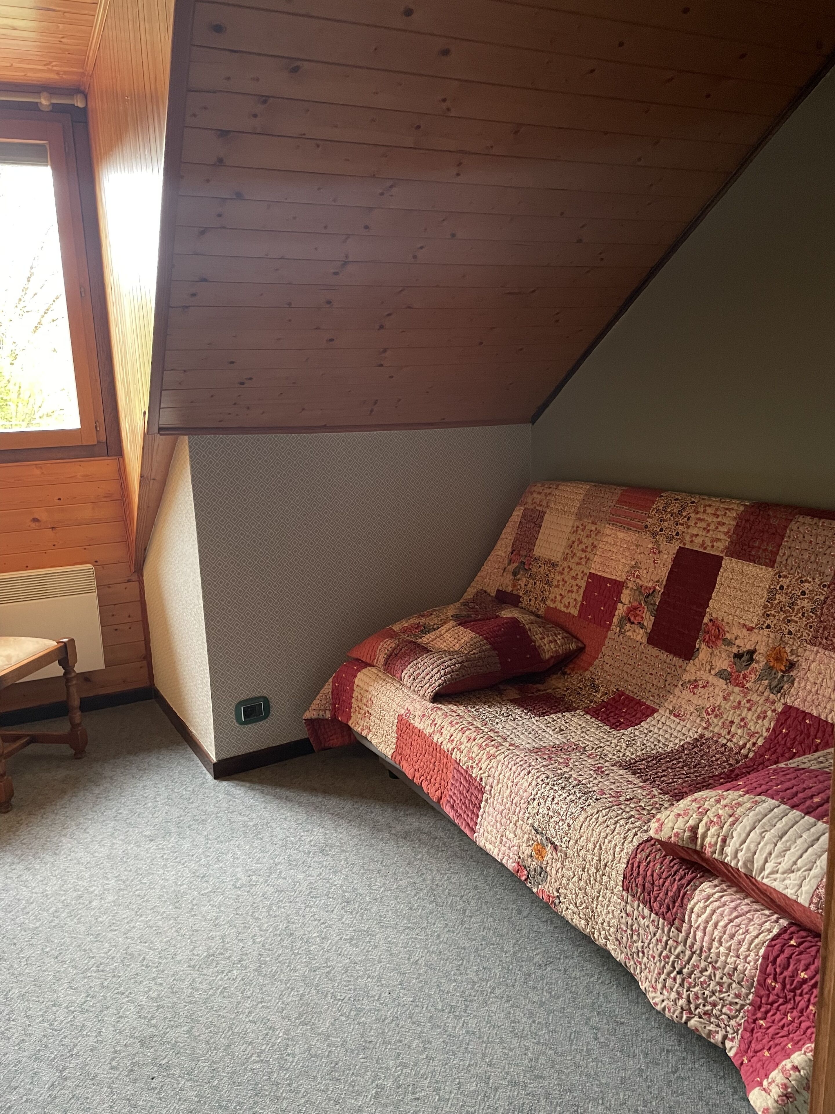 Une pièce chaleureuse avec un plafond en pente, un banc en bois, un lit recouvert d’une courtepointe et un radiateur.