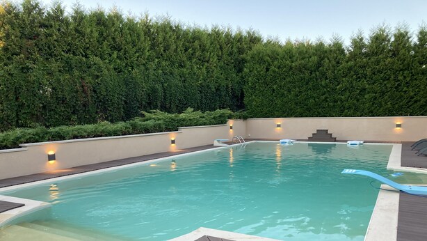 A rectangular swimming pool with a wooden deck, surrounded by a low wall and a dense green hedge. - Country property with covered terrace and large swimming pool (Charcier)