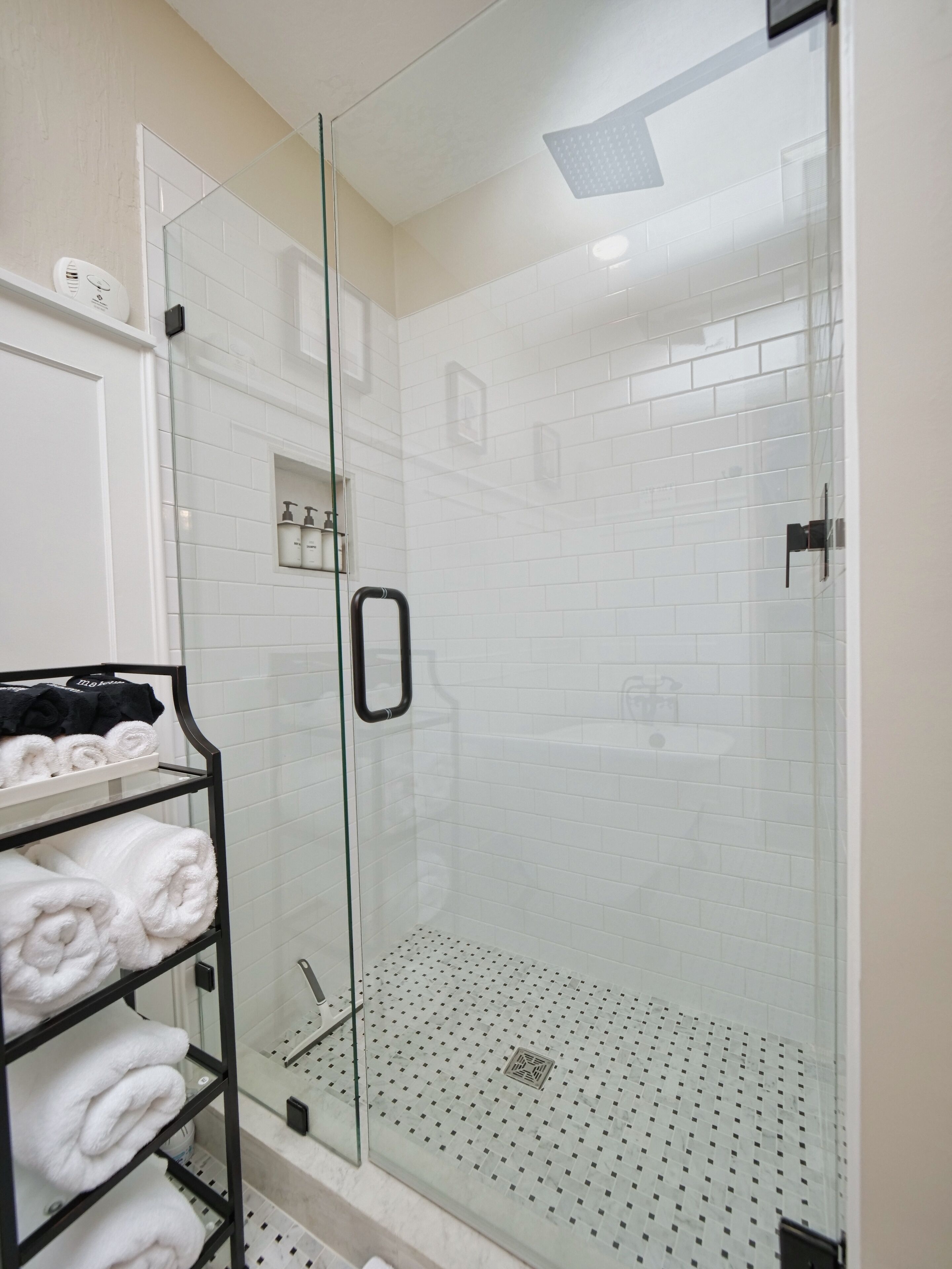 Eine begehbare Dusche mit Glaswand, Glastür und Ablage für Handtücher.