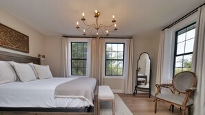 A bedroom with a large bed, a wooden headboard, a chandelier, a mirror, and a wooden chair. - Peaceful pet & family friendly MotherLode Cabin - steps to historic Sutter Creek (Sutter Creek)