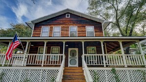 A two-story wooden house with a front porch, a flag, and a staircase leading to the entrance. - Peaceful pet & family friendly MotherLode Cabin - steps to historic Sutter Creek (Sutter Creek)