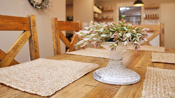A dining table with a white vase containing green and pink succulent plants, surrounded by wooden chairs and beige placemats. - Peaceful pet & family friendly MotherLode Cabin - steps to historic Sutter Creek (Sutter Creek)