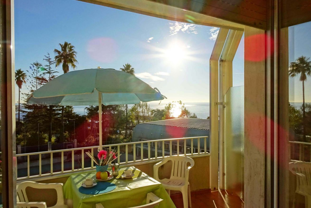 A balcony with a table set for two, a green tablecloth, and a blue umbrella.