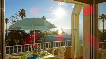 A balcony with a table set for two, a green tablecloth, and a blue umbrella.