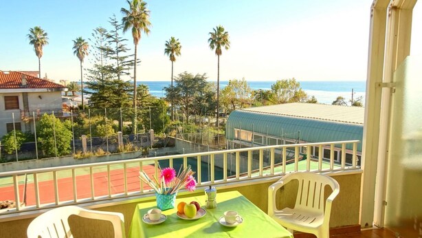 Un balcón con una mesa preparada para dos, con vista a una playa y palmeras.