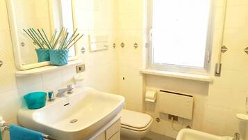 Une salle de bain équipée d’un lavabo, de toilettes, d’un bidet et d’une fenêtre.