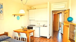 Una habitación pequeña con cama, una mesa de comedor con sillas, kitchenette y baño visible a través de una puerta abierta.