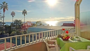 Un balcón con una mesa preparada para dos, con vistas a una piscina y palmeras.