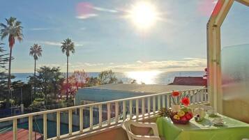 Un balcon avec une table dressée pour deux personnes, donnant sur une piscine et des palmiers.