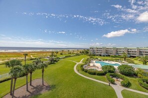 A resort with a pool, palm trees, and a view of the ocean. - Beautiful condo with the best views! (Saint Simons Island)