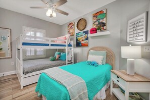A bedroom with bunk beds, a bed with a teal bedspread, a ceiling fan, and artwork on the walls. - Beautiful condo with the best views! (Saint Simons Island)
