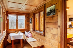 A wooden cabin interior with a dining table, bench, and windows overlooking a snowy landscape. - Vacation Home "Dünser" with Mountain View, on a sunny slope. (Bizau)