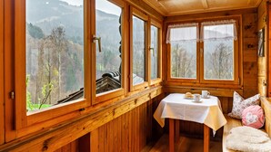 A wooden cabin with large windows, a table with cups and a plate, and a bench with pillows. - Vacation Home "Dünser" with Mountain View, on a sunny slope. (Bizau)