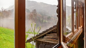 A view from a window with a wooden structure, a grassy area, and a hilly landscape. - Vacation Home "Dünser" with Mountain View, on a sunny slope. (Bizau)
