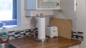 Een keuken met een houten aanrecht, een wit kastje met planken, een raam en een spoelbak.