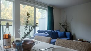 Een eetgedeelte met een tafel gedekt voor twee personen, een schaal, een fles wijn en een vaas met een plant.