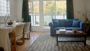 Een woonkamer met een bank, salontafel, eettafel met stoelen en een raam met gordijnen.