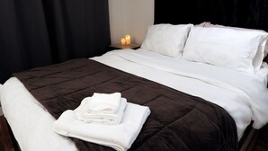 Een netjes opgemaakt bed met witte lakens, een bruin gewatteerd sprei en een gevouwen witte handdoek ernaast.